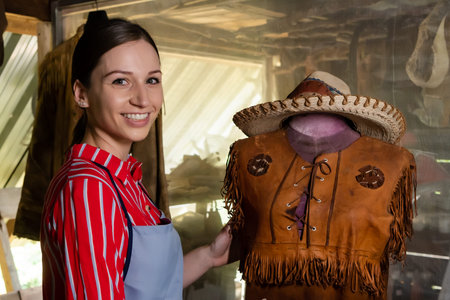 Women craftsman making leather by hand, using holding shirt made brown leather that is worn on...