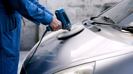 Close-up hand male mechanic wearing suit for working in garage for safety in risky work, mechanic standing using polishing machine scrub surface car that comes garage make new color.の写真素材