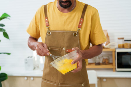 Closeup A bowl with several eggs being stirred together. A man is standing in the kitchen stirring eggs to prepare an omelet for breakfast. On days when working at home alone in the kitchenの写真素材