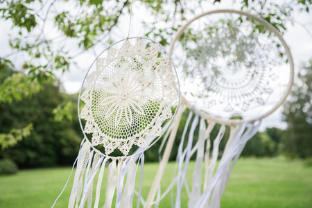 Delicate white dream catchers with green glade and trees on the background. The details of the wedding in boho styleの写真素材