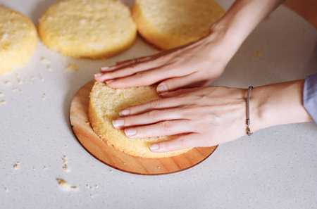 Woman stacking layers of sponge cake. Female hands in the frame. Series.