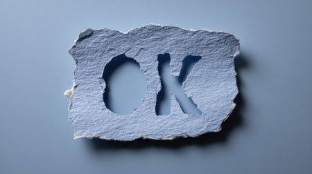 A piece of textured blue paper features the letters "OK" cut out, set against a matching background. The paper's rough edges create a sense of tactility, with even lighting and a straightforward composition. This image is suitable for various commercial uses, including advertising and graphic design projects.の素材
