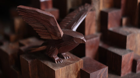 A detailed wooden sculpture of a bird is perched atop stacked wooden blocks. The artwork exhibits a rich brown color with visible wood grain texture. The composition utilizes a shallow depth of field, focusing on the bird and foreground blocks. Suitable for commercial projects or editorial use related to art.の素材