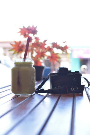 indonesia, 11-23-2020, sony a7 camera and nokia smartphone on a wooden table with a glass of fruit juice and red maple flowers in a pot, this photo can be used as a travel backgroundのeditorial素材