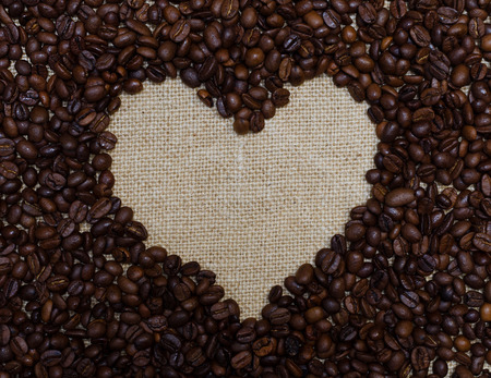 heart made with coffee beans stacked against burlap canvas.の写真素材