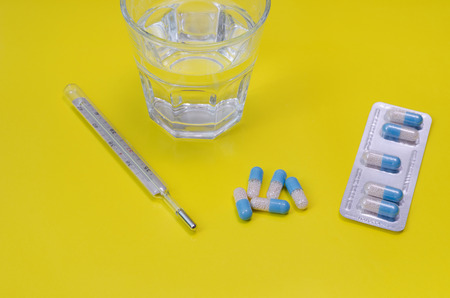 Water glass,  thermometer and medicaments on yellow background