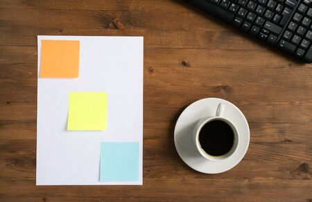 keyboard, colored stickers and cup of coffee laying on the board.