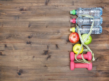 Healthy lifestyle concept. three colored Apples measuring tape dumbbells and sport  water bottles on  wooden tableの写真素材