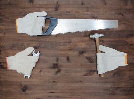 hacksaw hammer and gloves look like hands on old wooden tableの写真素材