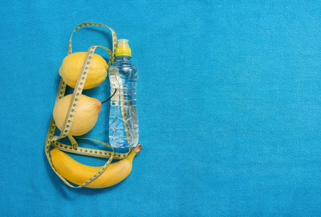Healthy lifestyle concept. measuring tape banana sports water pear and lemon  on blue towelの写真素材