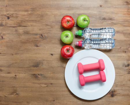 Healthy lifestyle concept. colored Apples dumbbells sport water bottles on wooden tableの写真素材