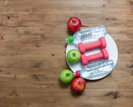 Healthy lifestyle concept. colored Apples dumbbells sport water bottles on wooden tableの写真素材