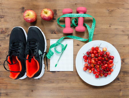 Fitness and diet concept. Sneakers notebook  apple cherries dumbbells and measure tapeの写真素材