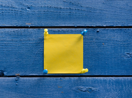 Yellow sticker and pins on old wooden wall