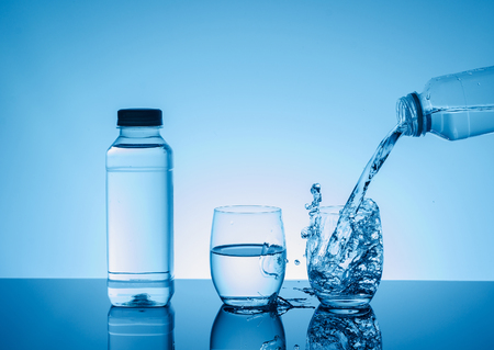 Bottle with creative splashing water in the glass on blue background.  