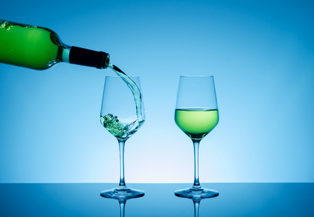 White wine pouring in glass on blue backgroundの写真素材