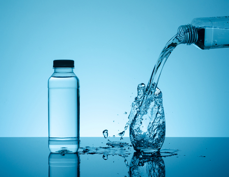 Bottle with creative splashing water in the glass on blue background.  の写真素材