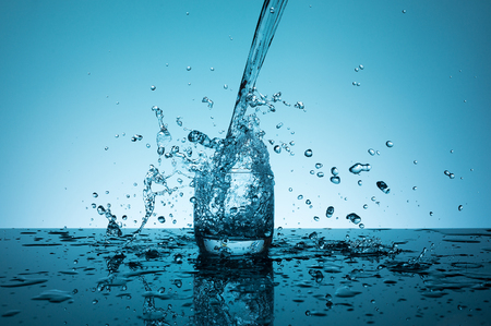Creative splashing water in the glass on blue background.の写真素材
