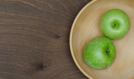 Two green apples in wooden bowl on tableの写真素材