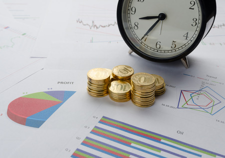 Business concept. Stack of coins, alarm clock and financial charts