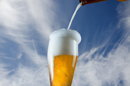 Pouring glass of beer from bottle on blue sky backgroundの写真素材