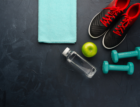 Fitness concept with sneakers dumbbells bottle of water and apple on black concrete backgroundの写真素材