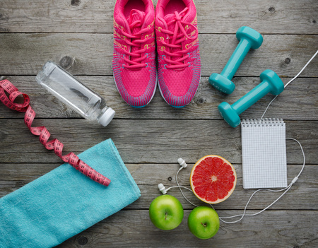 Fitness concept with sneakers dumbbells bottle of water apple pomelo and measure tape on old wooden table background の写真素材