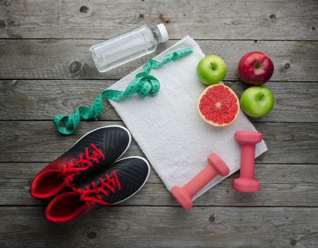 Fitness concept with sneakers dumbbells pomelo bottle of water apple and measure tape on old wooden table background の写真素材