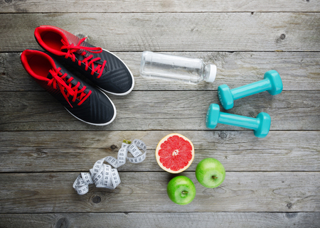Fitness concept with sneakers dumbbells pomelo bottle of water apple and measure tape on old wooden table backgroundの写真素材