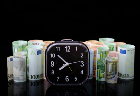 Alarm clock, and European paper money in rolls, on black background. Business concept, time is money.の写真素材