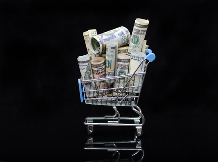 US dollars rolls and shopping cart full packs of bills on black background with reflection. Creative business and financial concept with usa dollar banknotes .の写真素材