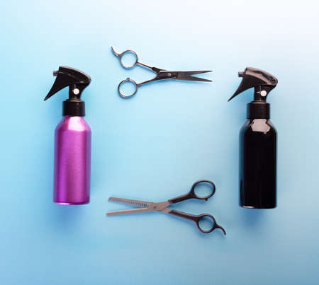 Spray bottles and scissors for haircut isolated on blue background, top view. Barber or hairdresser professional equipment. Hairstyle and hair care conceptの写真素材