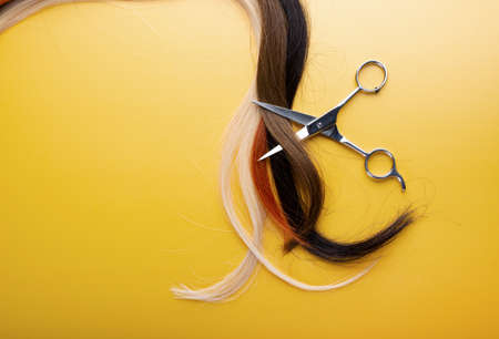 Professional hairstyle scissors with strands of hair isolated on yellow background. Hairdresser, beauty salon and barbershop service conceptの写真素材