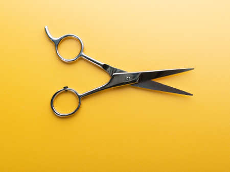 Professional haircutting scissors or shears isolated on yellow background. Haircut at home or in hairstyle salon or barber shop concept with hair cutting toolの写真素材