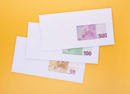 Stack of closed white envelopes with euro bills inside over yellow background. Concept of income,...