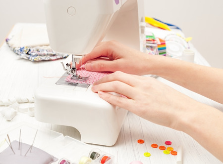 sewing, sewing on the sewing machine, sewing supplies, colored sewing threads, colored pieces of cloth, needles, centimeter, tailors scissors on white wooden backgroundの写真素材