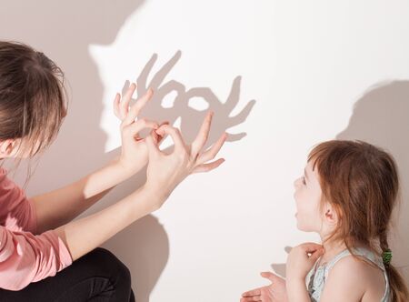 child plays with a parent in the theatre of shadows on a white wall