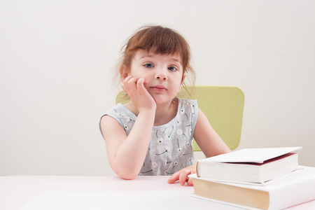 Girl sitting at table with books and looking right. Classes with the child.の写真素材
