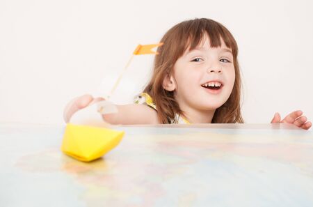 Girl playing with paper boat on painted map of the world. The girl enjoys the game and come up with their own rules. Place for text.の写真素材