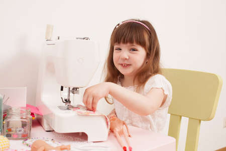 The girl is sewing on the sewing pieces of fabric on a pink table. Nearby are the needles, thread and buttons.の写真素材