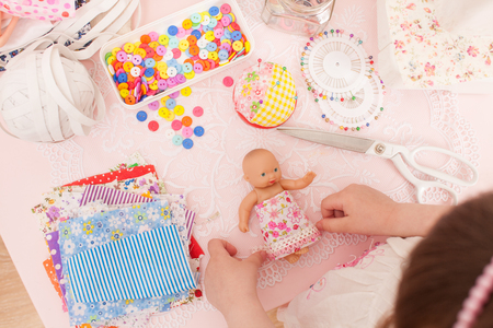 Girl playing fashion designer dressing the dolls in pieces of cloth. Next sewing machine, thread, buttons, needles, rubber and miscellaneous pieces of fabric.の写真素材