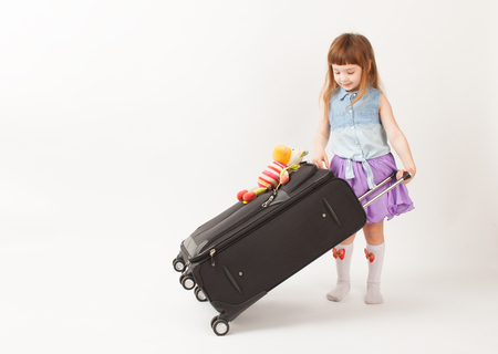 The girl is going on a trip with a large black suitcase on a white background. An empty space to insert text.の写真素材