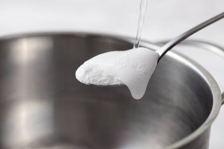 Baking soda slaked with vinegar in a spoon over a metal dish. Reaction between soda and vinegar with active foam.の写真素材
