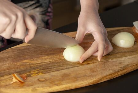 The cook cutting and dice onion on a wooden chopping board. Closeup.