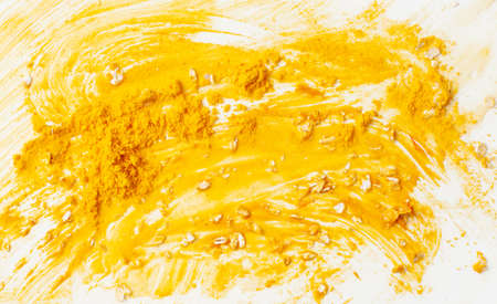 Bright yellow aromatic spice turmeric for health and beauty. Texture background of a smeared face mask made of turmeric, honey and oatmeal on a white. Copy space text.の写真素材