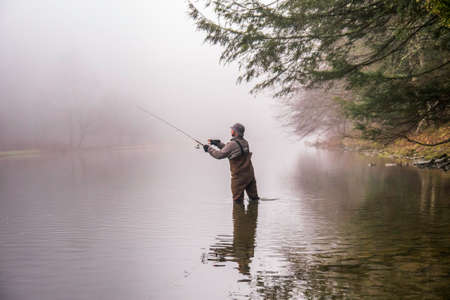 A fisherman wearing waders casts his fishing pole in a riverの写真素材