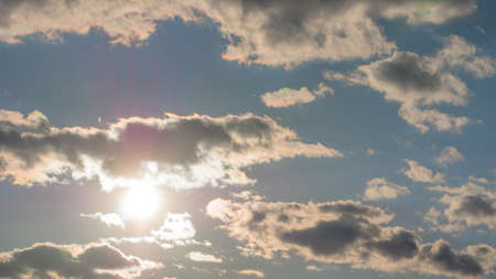 Sun peaking out behind clouds against a blue skyの写真素材