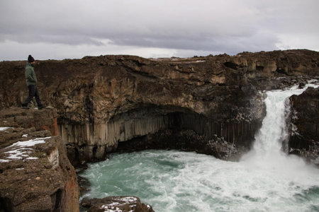 Man looking at the Aldeyjarfoss waterfall in northeastern Iceland surrounded by beautiful rock formations.の写真素材
