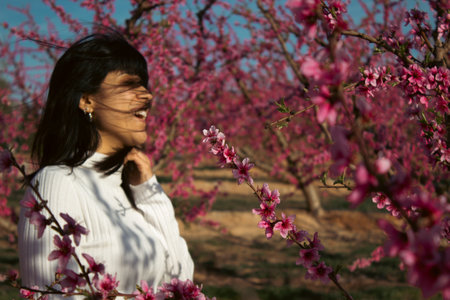 Woman smiling among fields of pink blossoming peach trees in springの写真素材