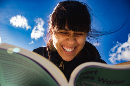 Beautiful smart woman reading a book and laughing in the green park outdoors